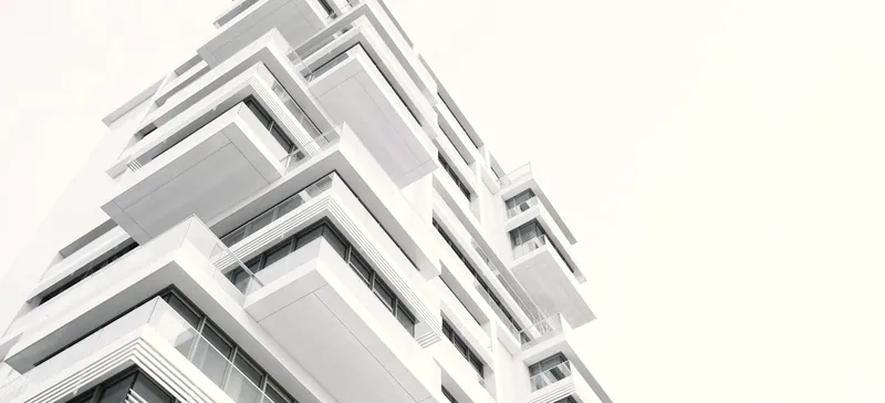 Immeuble blanc à balcons en gradins, vu en contre-plongée sur un ciel blanc.