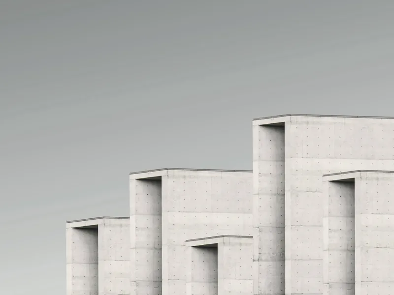 Façade en béton clair en gradins : trois volumes à fenêtres profondes, sous un ciel pâle.