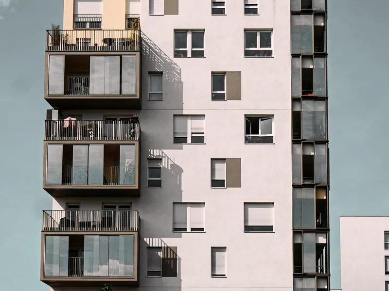 Immeuble blanc rosé à balcons vitrés, vu depuis la rue en contre-plongée.