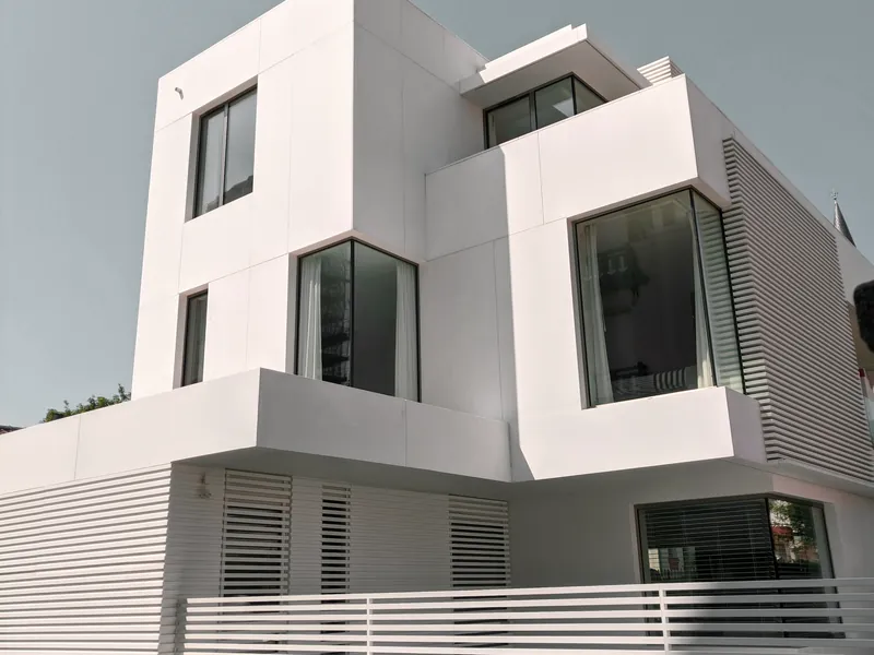 Maison cubique blanche à plusieurs niveaux, aux grandes baies vitrées et aux terrasses en saillie.